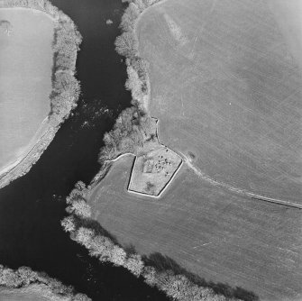 Oblique aerial view centred on the remains of the church and burial ground with the remains of a motte in trees adjacent, taken from the W.