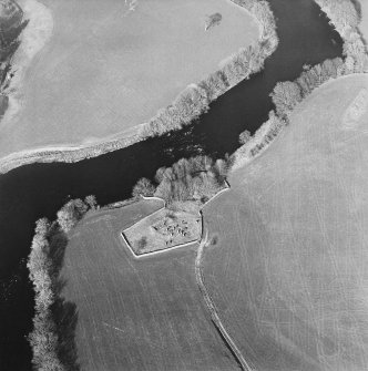 Oblique aerial view centred on the remains of the church and burial ground with the remains of a motte in trees adjacent, taken from the SW.