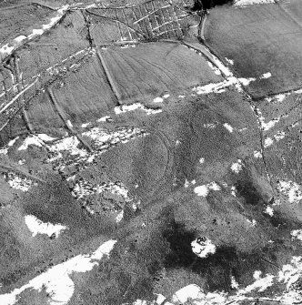 Raeburnfoot, oblique aerial view, taken from the NNW, centred on a bank barrow, an enclosure and field banks.