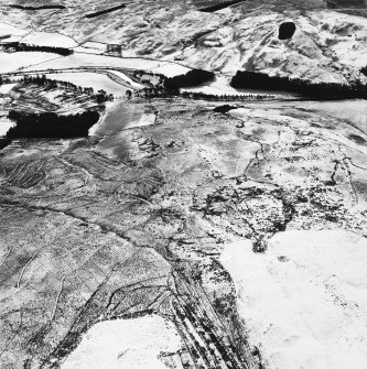 Raeburnfoot, oblique aerial view, taken from the NNE, centred on a bank barrow, with ring-enclosures, enclosures and a Roman Fort to the left of the photograph.