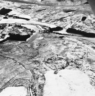 Raeburnfoot, oblique aerial view, taken from the N, centred on a bank barrow, with ring-enclosures, enclosures and a Roman Fort to the left of the photograph.