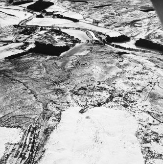 Raeburnfoot, oblique aerial view, taken from the NNW, centred on a bank barrow, with ring-enclosures, enclosures and a Roman Fort to the left of the photograph.