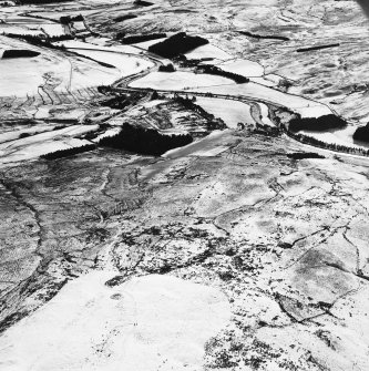 Raeburnfoot, oblique aerial view, taken from the NW, centred on a bank barrow, with ring-enclosures, enclosures and a Roman Fort to the top of the photograph.