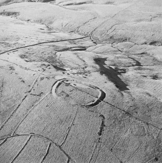 Oblique aerial view of Kirk Hill centred on the remains of a fort and palisaded enclosure with a farmstead, field-system, rig and boundary banks and buildings, enclosures, lazy-beds and quarries adjacent, taken from the E.
