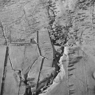 Oblique aerial view of Ettleton Sike centred on a burial ground with a building, field-system, rig and sheepfold and hut, field-system, rig and enclosure adjacent, taken from the ESE.