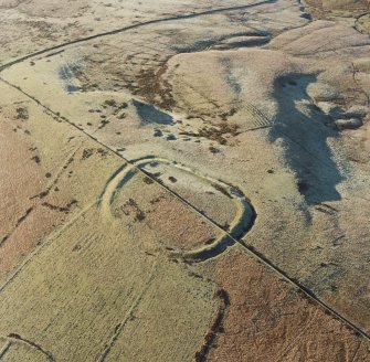 Oblique aerial view of Kirk Hill centred on the remains of a fort and palisaded enclosure with the remains of buildings, enclosures, lazy-beds, quarries, a farmstead, field-system, rig and boundary banks adjacent, taken from the E.