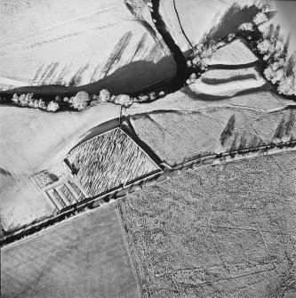 Oblique aerial view of Castleton centred on a burial ground and remains of a church with the remains of an earthwork fortification adjacent, from S.