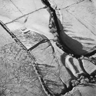 Oblique aerial view of Castleton centred on a burial ground and remains of a church with the remains of an earthwork fortification adjacent, from E.