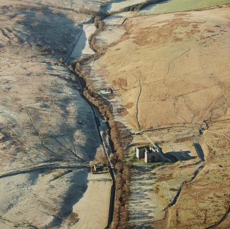 Oblique aerial view of Hermitage Castle centred on the remains of a castle and earthwork castle with the remains of a chapel, moated site and boundary dyke adjacent, taken from the E.
