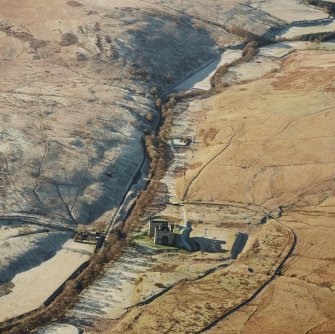 Oblique aerial view of Hermitage Castle centred on the remains of a castle and earthwork castle with the remains of a chapel, moated site and boundary dyke adjacent, taken from the ENE.