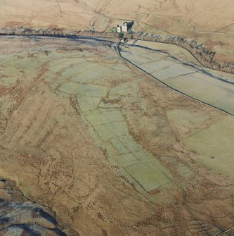 Oblique aerial view of Toft Knowes centred on the remains of a field-system, rig and pens with the remains of a farmstead, quarries and settlement adjacent and Hermitage Castle in the background, taken from the S.