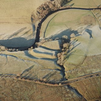 Oblique aerial view of Liddel Castle centred on the remains of an earthwork fortification, taken from the SSE.