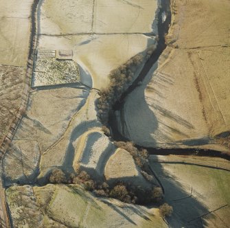 Oblique aerial view of Liddel Castle centred on the remains of an earthwork fortification and burial-ground, from NE.