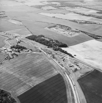 Oblique aerial view centred on the road construction and the quarry, with the farmhouses, farmsteading and cottages adjacent, taken from the ESE.
