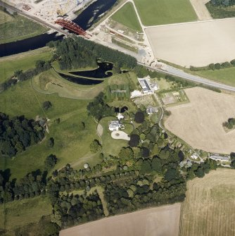 Oblique aerial view centred on the country house and garden with the lodge, railway viaduct and construction works adjacent, taken from the SW.