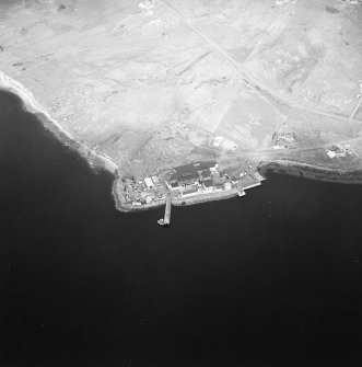 Oblique aerial view centred on the factory and laboratory with the pier and remains of lazy beds adjacent, taken from the S.