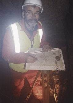 Commission at work: Mr I Parker with plane table on half-landing of subterranean structure.
