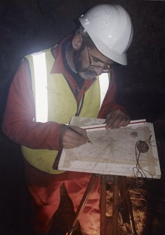 Commission at work: Mr I Parker with plane table on half-landing of subterranean structure.