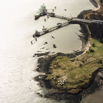 Oblique aerial view of Charles Hill centred on the remains of a coast battery and military camp with a ferry-house cellar adjacent and the piers for gas loading in the background, taken from the NE.