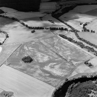 Oblique aerial view centred on the cropmarks of an enclosure and trackways with round house, enclosure, pits, cultivation remains, pit-alignment and long barrow adjacent, taken from the SE.