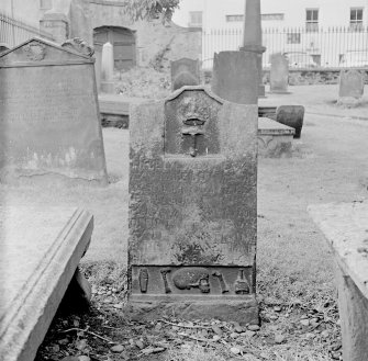 View of tombstone in St Mary's Church burial ground, Banff, with emblem of guild of hammermen at the top. Along bottom are these symbols: coffin, two bones either side of skull and deid bell.