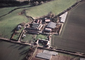 Oblique aerial view centred on the farmhouse and farmsteading, taken from the NW