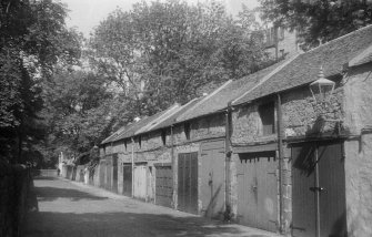 General view of the coach houses on Meadow Lane, Edinburgh, seen from the East South East with the rear of the South side of Buccleuch Place in the background partially obscured by trees.