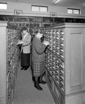 Interior.  View within library showing wooden cabinets containing drawers of index cards, cross-referencing Reports with reference books and journals.  A large part of the library's holdings was sent to ICI Explosives headquarters in Australia in 1996, but the Index remained in Ardeer.  Also in the picture are Annette Kelly (right, Information Officer) and Sheila Conway (former Records and Reports Officer)