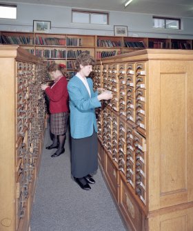 Interior.  View within library showing wooden cabinets containing drawers of index cards, cross-referencing Reports with reference books and journals.  A large part of the library's holdings was sent to ICI Explosives headquarters in Australia in 1996, but the Index remained in Ardeer.  Also in the picture are Annette Kelly (left, Information Officer) and Sheila Conway (former Records and Reports Officer)