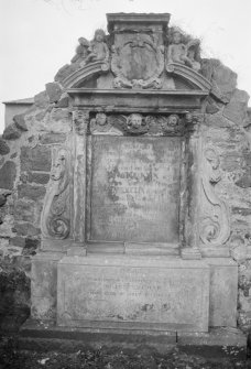 View of mural monument commemorating Robert Kirkwood d. 1730 in the churchyard of North Berwick Church, showing reclining putti holding palm fronds on tympanum slopes and inscription panel flanked by Corinthian pillasters, and three winged cherubs above.
