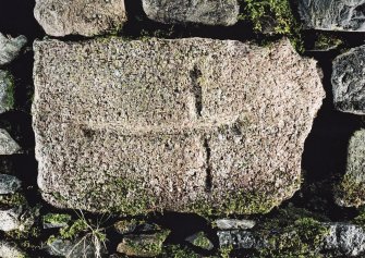 Photograph of cross-incised stone built into wall of farm building.