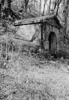 General view of exterior of well house, Bealach an Fhuarain, Inveraray Castle Estate, showing small stone building with pediment and vermiculated rustication over the arch entrance.