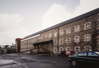 Selkirk, Dunsdale Haugh, Dunsdale Road, Riverside Mills
View from north east of south east side of original spinning mill, with the engine-house in the background. At the time of the survey, the mill was used predominantly as a warehouse, and a mobile chute can be seen permitting the rapid loading of lorries