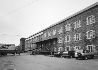 Selkirk, Dunsdale Haugh, Dunsdale Road, Riverside Mills
View from north east of south east side of original spinning mill, with the engine-house in the background. At the time of the survey, the mill was used predominantly as a warehouse, and a mobile chute can be seen permitting the rapid loading of lorries, one of which is visible (left)