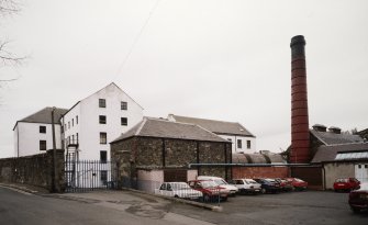 General view of mill from NE, showing high mill block, left, and boilerhouse and chimney, right.