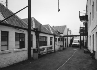 View from E along passage between offices and single storeyed sheds, left and high mill, right.