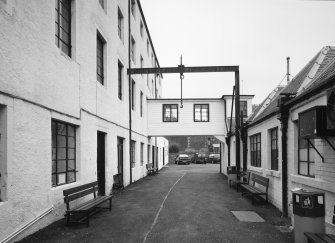View from W along passage between offices and single storeyed sheds, right, and high mill, left.