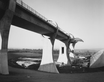 Oblique view from SSE along E side of Falkirk Wheel Union Canal aqueduct, with empty canal basin in foreground, and visitor centre (right)