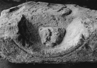 View of dressed sandstone block with coped sides and bearing a cat like head in high relief, held in the garage behind the manse.