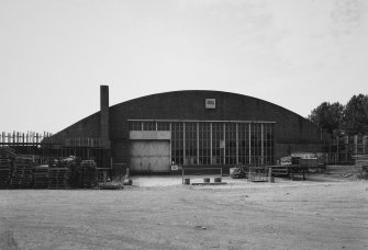 View from NE of NNE end of hangar, showing brick gable with windows and door and brick chimney stack		