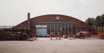 View from NNE end of hangar, showing brick gable with windows and door, and brick chimney stack