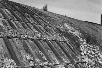 Detailed view from SE of centre part of hangar, showing exposed fabricated steel shell (left), with adjacent relatively intact outer layer of concrete, covered with bitumen