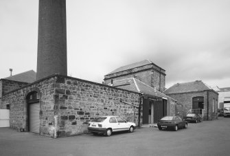 General view from SE of SE corner of works, showing boiler-house 		chimney, boiler house and former engine house
