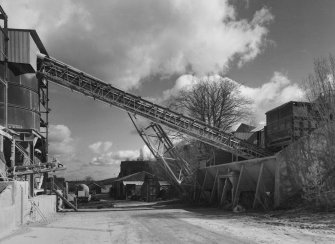 View from W showing overhead conveyor from primary crusher (base visible to right) to former shaft kilns (now storage hoppers to left).  The supporting strut for the conveyor is a surviving portion of one of the original conveyors supplying the shaft kilns