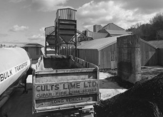 View from W of W end of lime works, showing road haulage vehicles in foreground, and dispatch hoppers in background