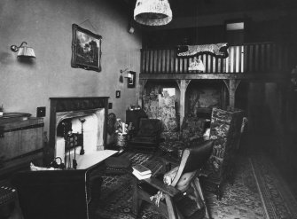 View of drawing room showing fireplace, items of furniture and wooden balcony in the background.