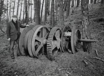 View from S of the remains of a steam-winding engine belonging to an earlier shaft of the mine (NS42SW 19.01), now situated in adjacent woodland at NS 4316 2330.  The owner of the mine, Kenneth Montgomerie, is helping to scale the object.