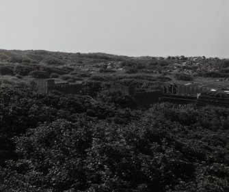 Elevated general view from NNE (on Nitroglycerine Hill No. 2 (NE, NS23NE 1.03]) of shells of Catridging Houses (AZF4) to right, connected by ropeway-gantry (the end of which is visible to the right). the rubble in the background is the remains of recently demolished magazines