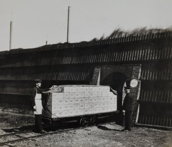 Photographic copy of view showing part of Blasting Department with a fully loaded. Bogey (wagon) with finished cases of gelignite leaving Packing House (G282) for storage magazines