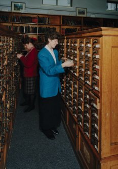 Interior.  View within library showing wooden cabinets containing drawers of index cards, cross-referencing Reports with reference books and journals.  A large part of the library's holdings was sent to ICI Explosives headquarters in Australia in 1996, but the Index remained in Ardeer.  Also in the picture are Annette Kelly (left, Information Officer) and Sheila Conway (former Records and Reports Officer)
